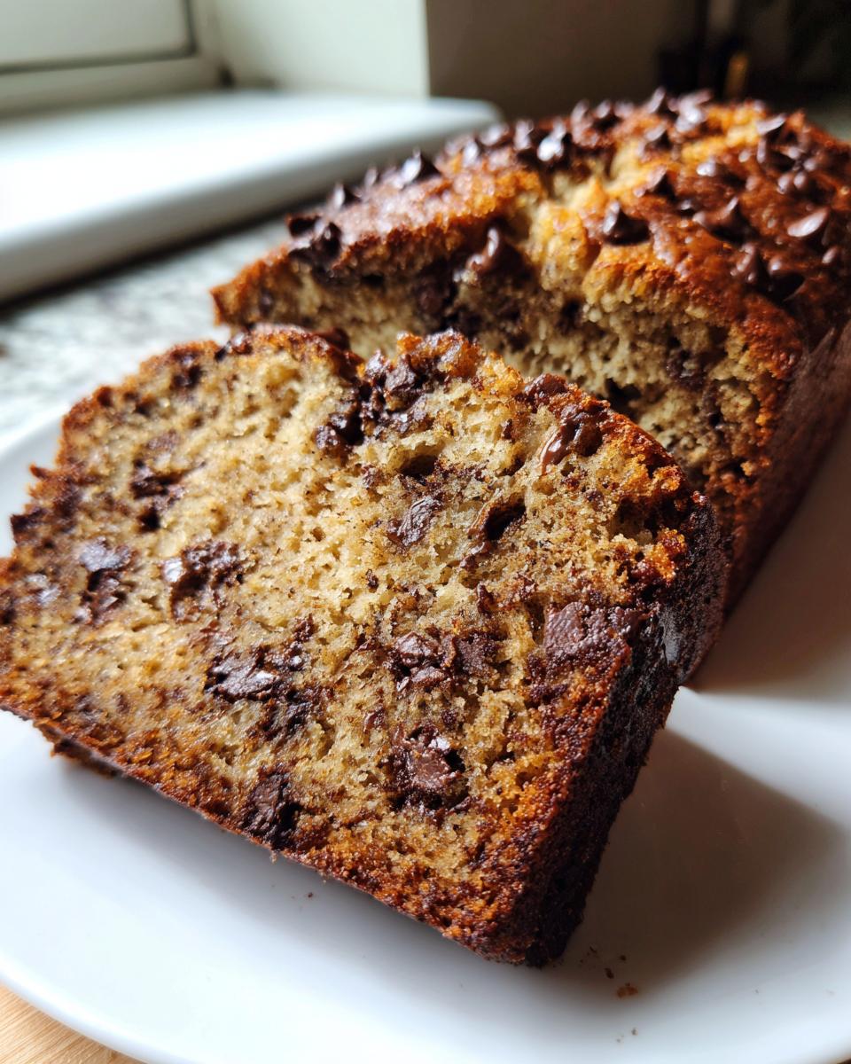 A thick slice cut from a moist chocolate chip banana bread recipe, showing rich texture and melted chips.