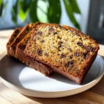 Three thick slices of moist chocolate chip banana bread displayed on a light gray plate.
