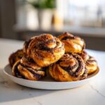 A stack of freshly baked chocolate cinnamon crunch knots with a sugary topping on a white plate.