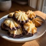 A stack of golden italian butter cookies, piped into star shapes and dipped in dark chocolate, resting on a light plate.