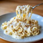 A fork lifting strands of creamy pasta coated in rich cottage cheese alfredo sauce, topped with grated cheese.