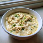 Close-up of a white bowl filled with creamy keto white chicken chili, topped with shredded chicken and green onions.