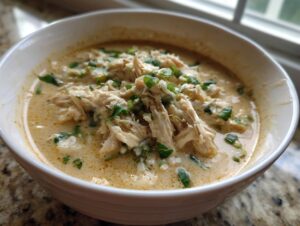 Close-up of a white bowl filled with creamy keto white chicken chili, topped with shredded chicken and fresh green herbs.