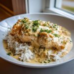 Close-up of creamy smothered chicken and rice served in a white bowl, topped with fresh parsley.