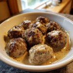 A white bowl filled with perfectly browned, juicy swedish meatballs smothered in a rich, creamy gravy.