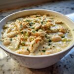 Close-up of a white bowl filled with creamy white chicken chili recipe, featuring shredded chicken and white beans.