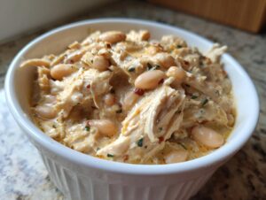 Close-up of creamy white chicken chili recipe featuring shredded chicken and white beans in a white bowl.