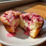 A delicious crumbl raspberry cheesecake cookie cut in half showing the creamy center and raspberry filling.