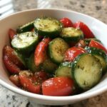 Close-up of a vibrant cucumber tomato salad tossed in a light vinaigrette and herbs, served in a white bowl.