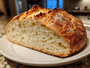 A close-up of a freshly baked dutch oven no knead crusty bread, showing the airy interior crumb and golden-brown crust.