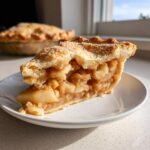 Close-up of a thick slice of amazing apple pie showing flaky crust and cinnamon-spiced apple filling.