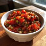 Close-up of chunky, fresh homemade salsa recipe featuring diced tomatoes and cilantro in a white bowl.