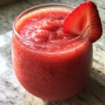 Close-up of a vibrant, frozen strawberry daiquiri garnished with a fresh strawberry slice.