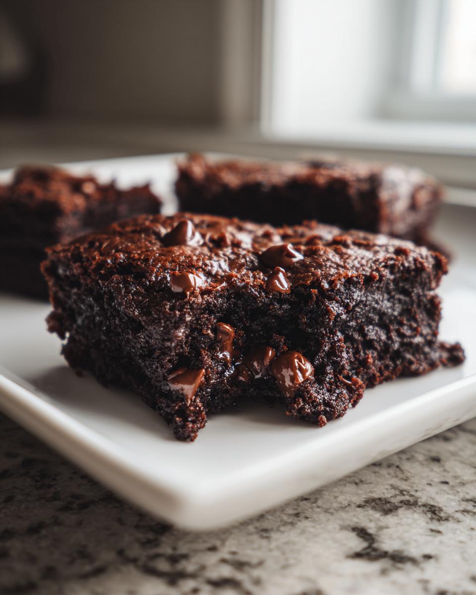 Close-up of a fudgy black bean brownies square topped with melted chocolate chips on a white plate.