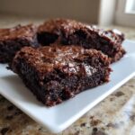 Close-up of fudgy black bean brownies on a white plate, showing a melted chocolate chip inside the rich, dark center.