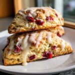 Two stacked, freshly baked cranberry orange scones topped with a thick, dripping vanilla glaze.