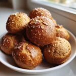 A stack of golden brown, round high-protein high-fiber pretzels topped with coarse salt crystals on a white plate.
