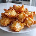 A pile of crispy, golden brown homemade crab rangoons with creamy filling visible, served on a white plate.