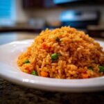 A close-up, appetizing shot of a mound of vibrant orange homemade Mexican rice mixed with bright green peas and diced carrots.