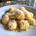 A close-up of freshly made homemade soft pillowy gnocchi served on a white plate and generously topped with grated Parmesan cheese.