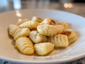 A close-up of freshly made homemade soft pillowy gnocchi lightly browned and dusted with grated cheese in a white bowl.
