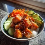 Close-up of a delicious salmon bowl featuring honey-glazed salmon cubes over rice, topped with sesame seeds, sliced avocado, cucumber, and shredded carrots.