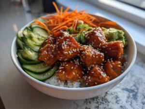 A close-up of a delicious honey glazed salmon bowl served over rice with sliced cucumbers, shredded carrots, and avocado.