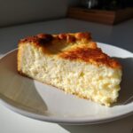 A thick slice of creamy Italian ricotta cheesecake recipe with a beautifully browned top, served on a white plate.