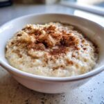 A close-up of creamy Jamaican cornmeal porridge with coconut milk, topped generously with ground cinnamon.
