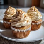 Three moist banana cupcakes with tall swirls of cream cheese frosting dusted generously with cinnamon.