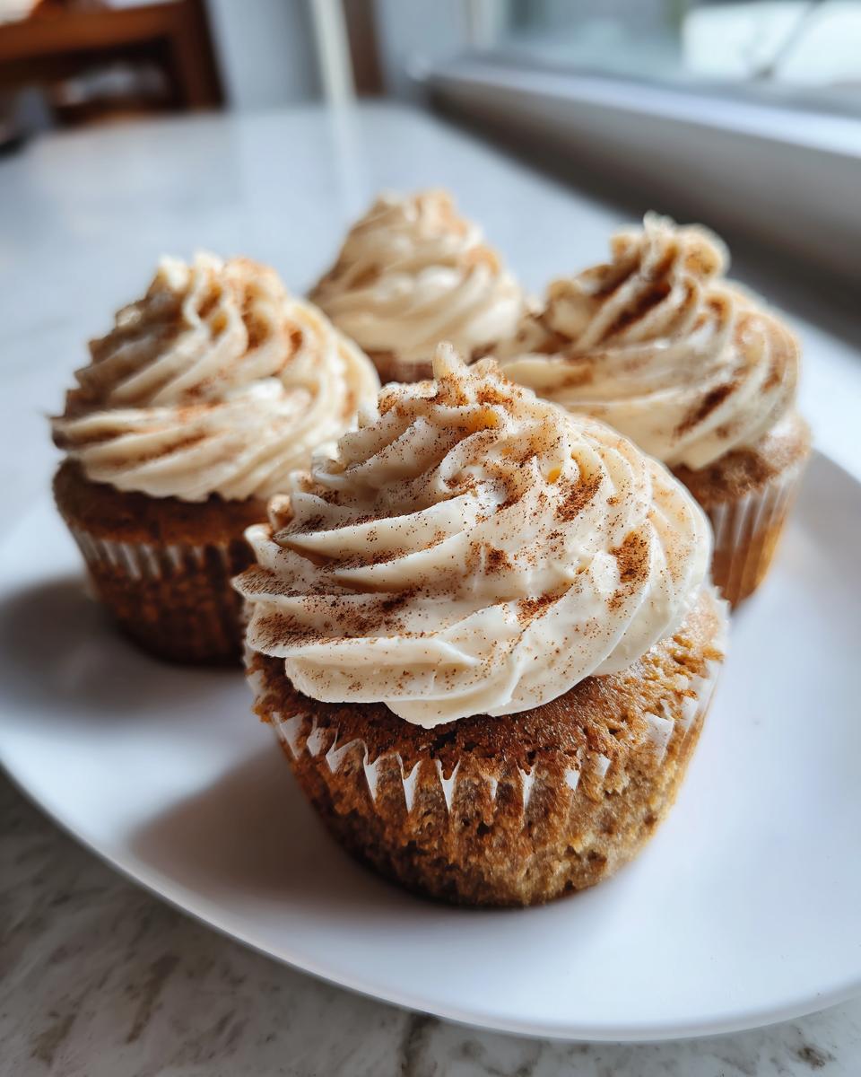 Four perfectly baked banana cupcakes topped with creamy frosting and a dusting of cinnamon.