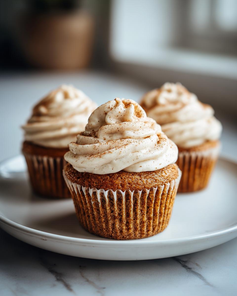 Close-up of a moist banana cupcakes topped with swirled frosting and a sprinkle of cinnamon.