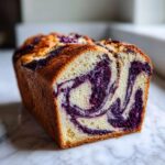 Cross-section of a moist blueberry bread loaf showing a beautiful purple swirl pattern in the crumb.