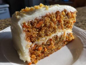 Close-up of a moist slice of carrot cake layered with cream cheese frosting and topped with crumbs.
