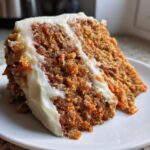 Close-up of a moist slice of carrot cake showing shredded carrots and thick cream cheese frosting.
