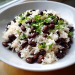 A close-up of a white bowl filled with fluffy white rice mixed with savory black beans and topped with fresh chopped cilantro.