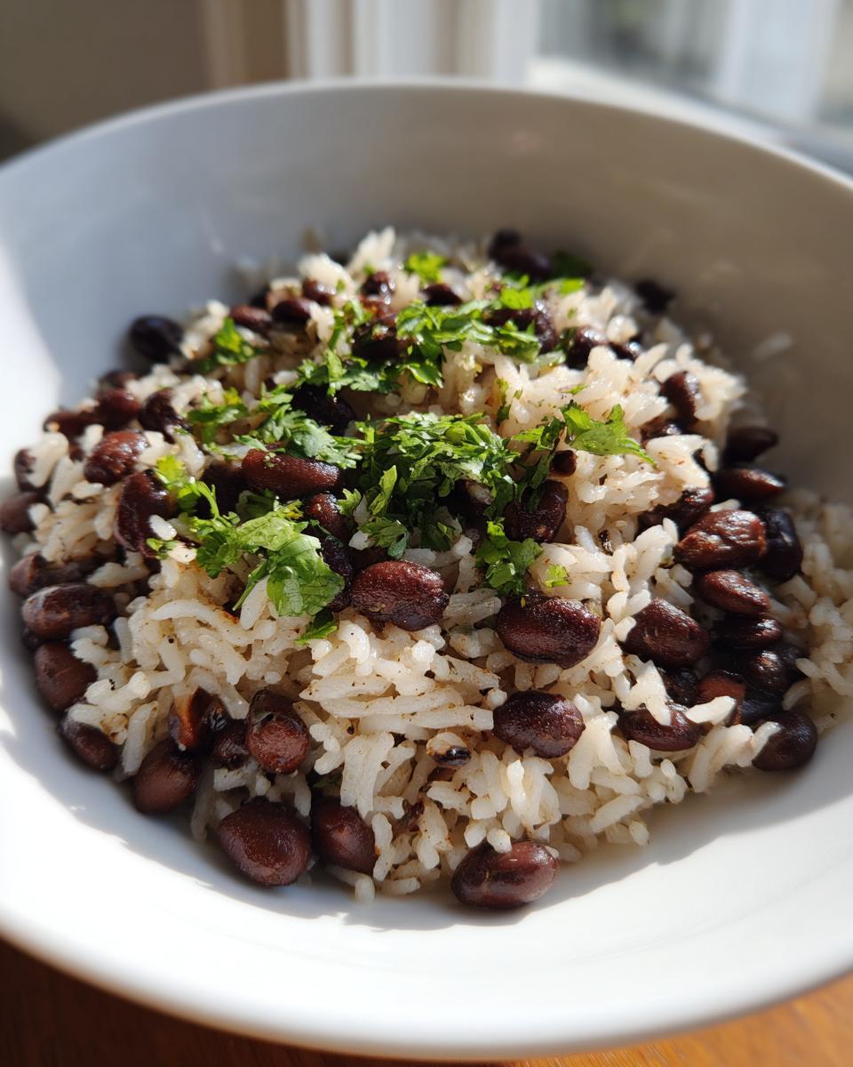 Close-up of a white bowl filled with fluffy white rice mixed with dark black beans and topped with fresh cilantro.