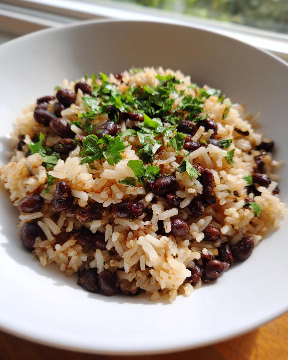 Close-up of a white bowl filled with seasoned black beans and rice, topped generously with fresh chopped parsley.