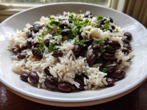 Close-up of a white bowl filled with fluffy white rice mixed with dark black beans and topped with fresh cilantro.