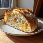 Cross-section of a slice of parmesan garlic artisan bread showing a light, airy crumb dotted with melted cheese.
