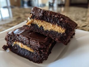 Two rich, dark chocolate peanut butter stuffed brownies stacked on a white plate, showing the creamy filling.