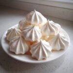 A stack of perfectly piped, crisp white meringue cookies piled high on a small white plate.
