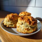 Three freshly baked pistachio pudding mix scones with golden tops sitting on a light gray plate.