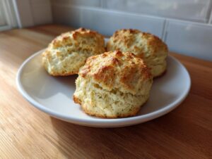 Three golden-brown pistachio pudding mix scones stacked on a small white plate, ready to eat.