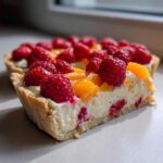 Close-up of a slice of raspberry mango tart showing the creamy filling and fresh fruit topping.