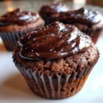 Close-up of a moist chocolate cupcake topped with glossy dark chocolate frosting and sparkling sugar crystals, part of a batch of raspberry chocolate cupcakes.