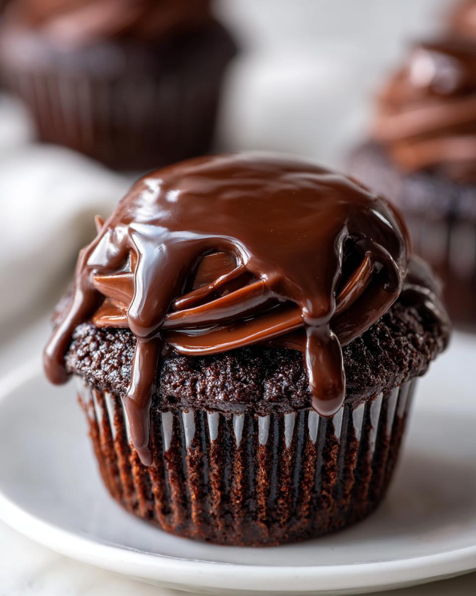 Close-up of a rich chocolate cupcake topped with dark chocolate frosting and a glossy chocolate ganache drip, perfect for raspberry chocolate cupcakes.