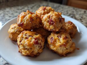A pile of golden brown rotel cream cheese sausage balls with visible melted cheese and diced red peppers on a white plate.