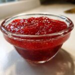 Close-up of vibrant red strawberry freezer jam served in a small, clear glass bowl.