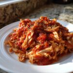 A serving of shredded crockpot italian chicken mixed with chunky tomato sauce and topped with herbs.